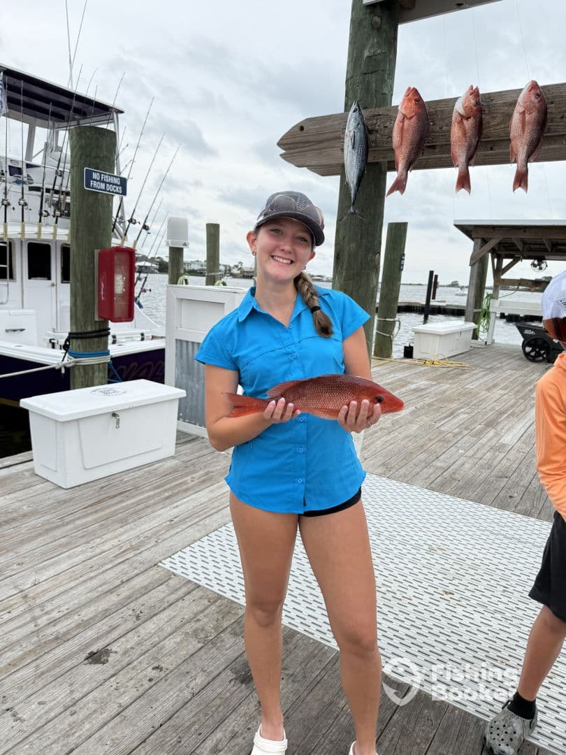 A young angler proudly displaying a Red Snapper at the dock, with a fishing boat in the background.