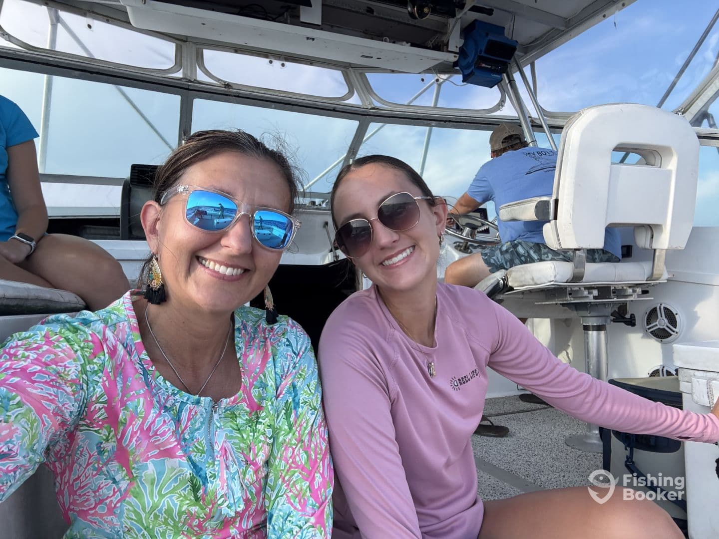 Two women enjoying a moment inside the boat, showcasing the comfortable seating and helm area during a fishing trip.