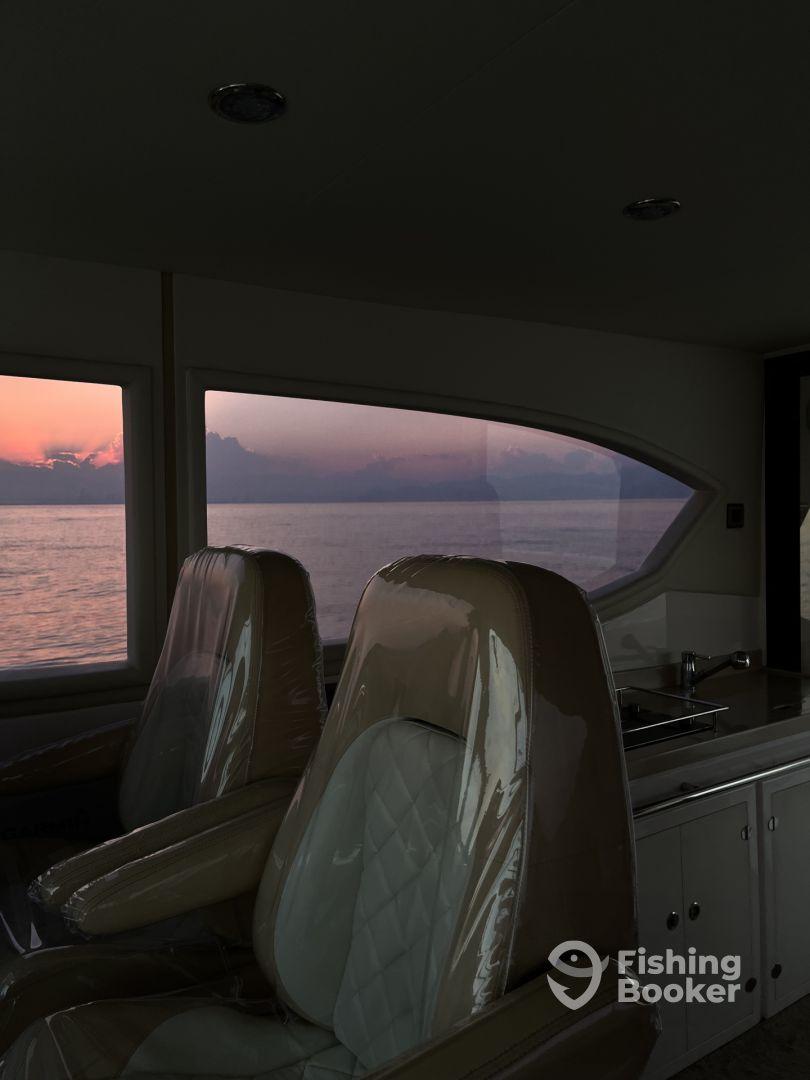 Interior view of a modern fishing boat showcasing plush seating and a serene sunset over the water.
